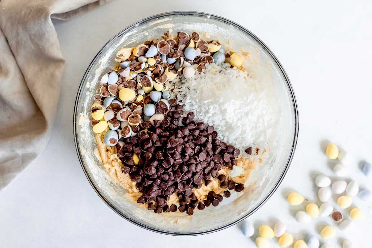 blondie dough with chopped Cadbury mini eggs, coconut, and chocolate chips in glass mixing bowl.