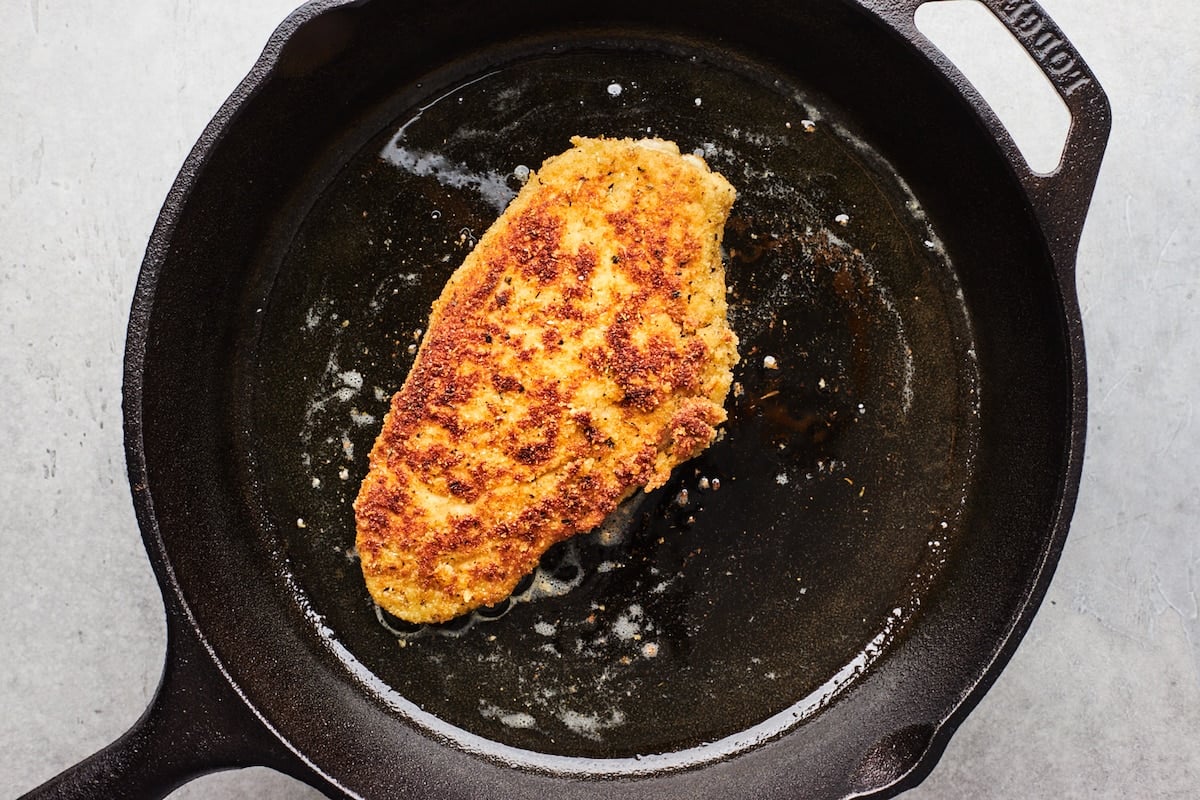 chicken parmesan frying in cast iron skillet.