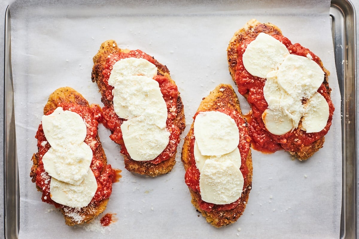 chicken parmesan with marinara sauce and mozzarella cheese on large baking sheet with parchment paper.