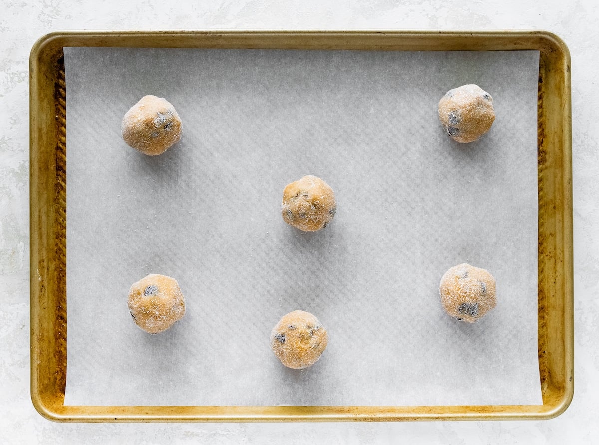 peanut butter chocolate chip cookie dough balls rolled in sugar and placed on baking sheet with parchment paper.