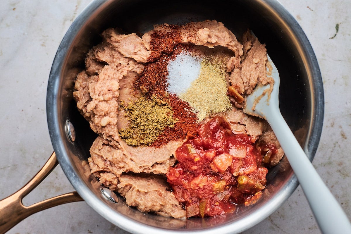 refried beans, salsa, and spices in pan with spatula.