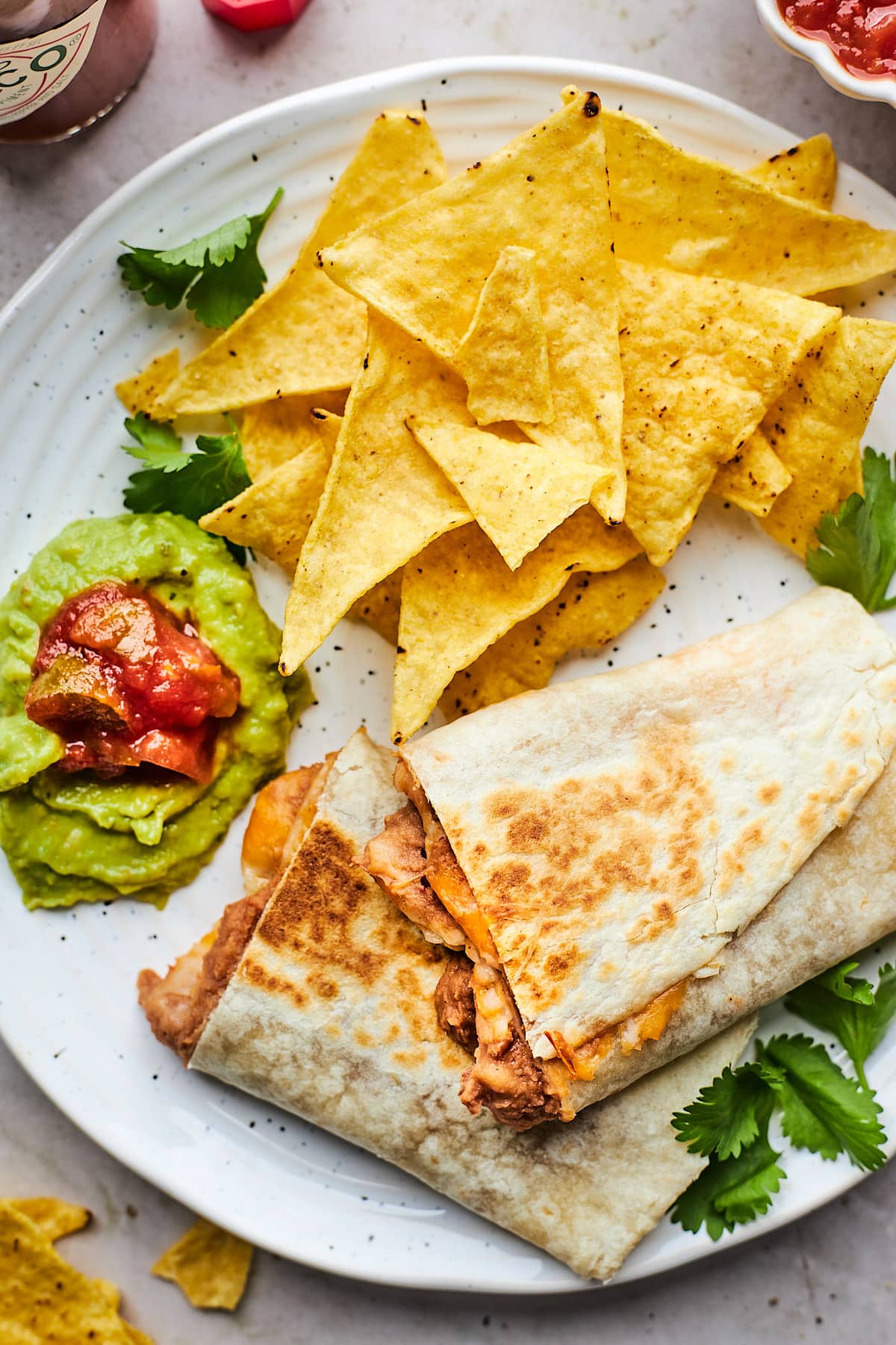 bean and cheese burrito cut in half on plate with chips, salsa, and guacamole.