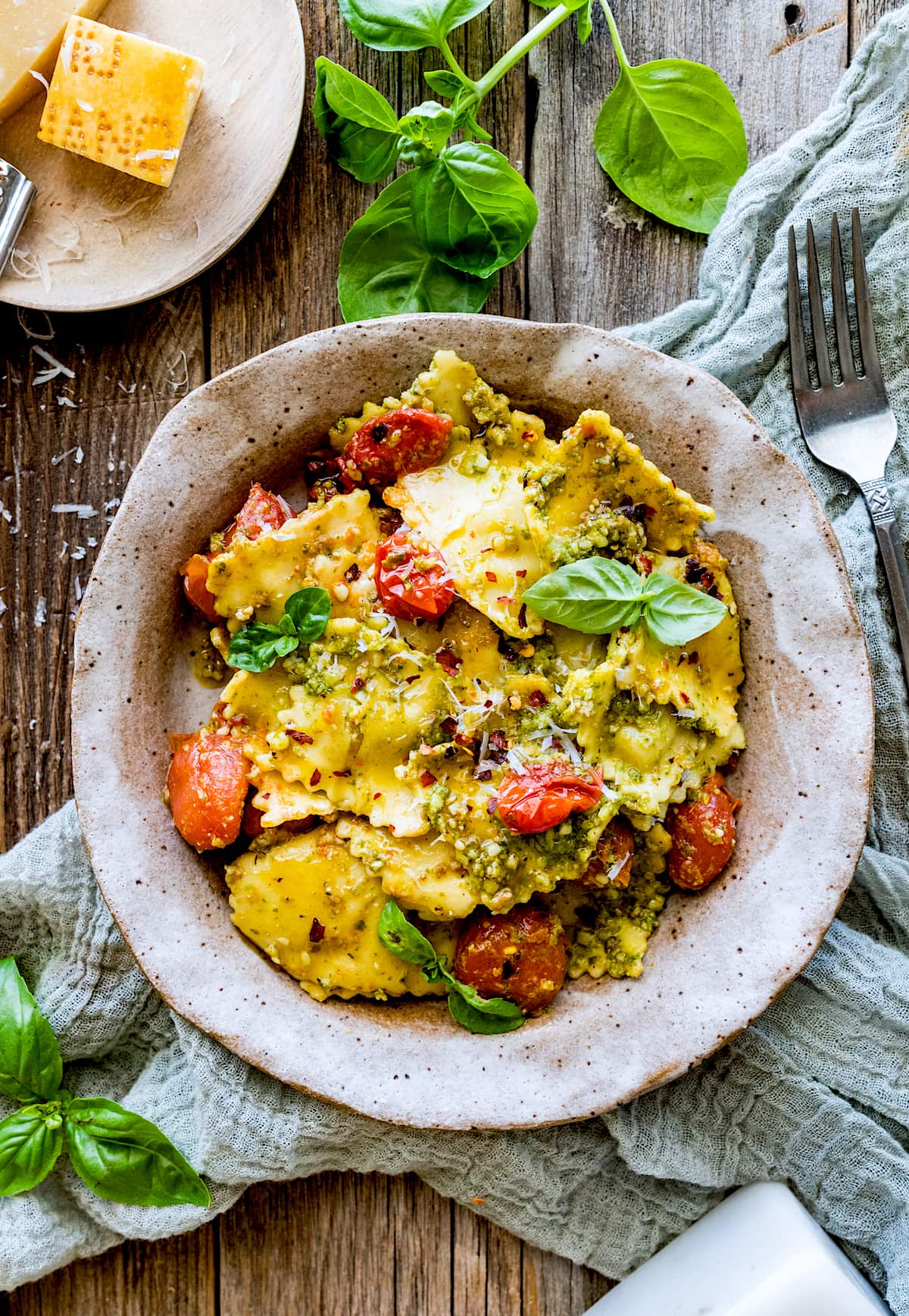 pesto ravioli in bowl with tomatoes, basil, and Parmesan cheese.
