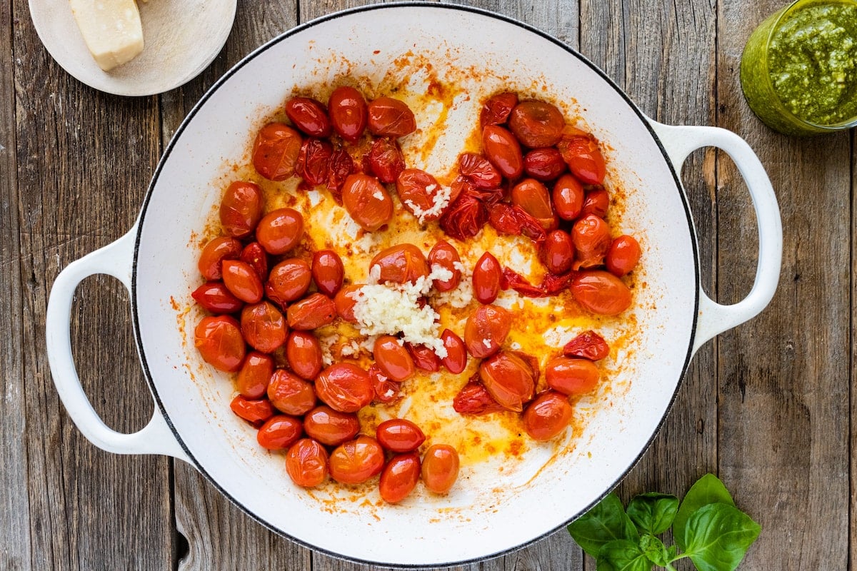 grape tomatoes cooking with garlic in large white pot.