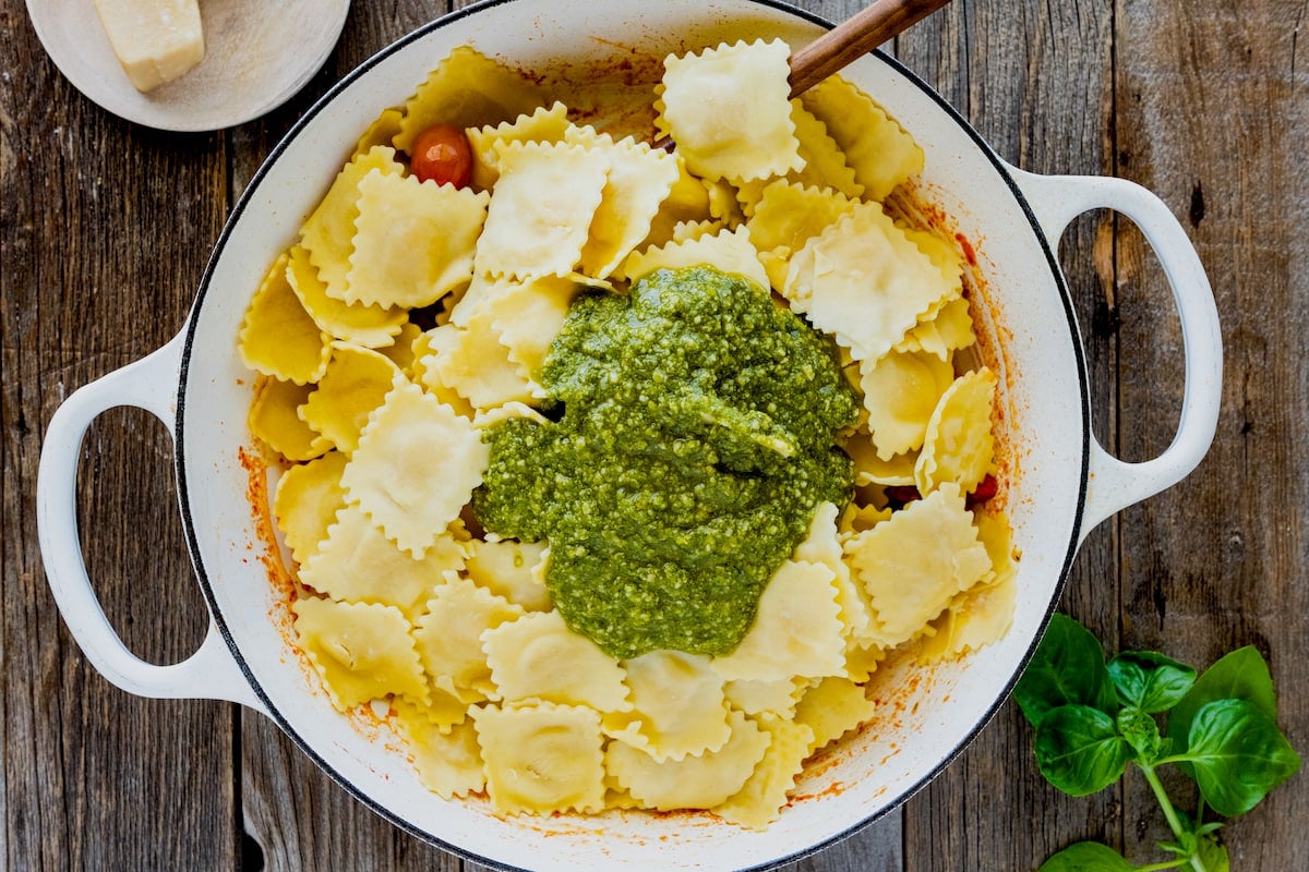 cheese ravioli with basil pesto in large pot with wooden spoon.