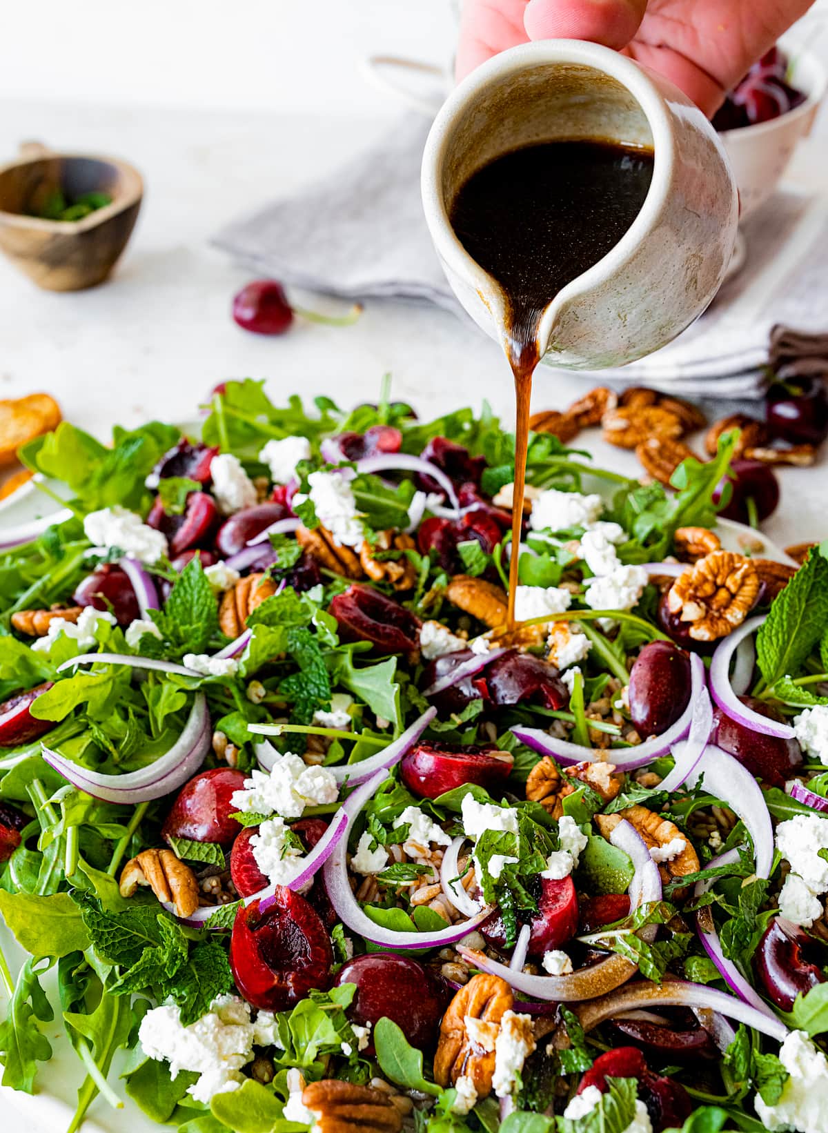 balsamic vinaigrette being poured over cherry arugula farro salad.