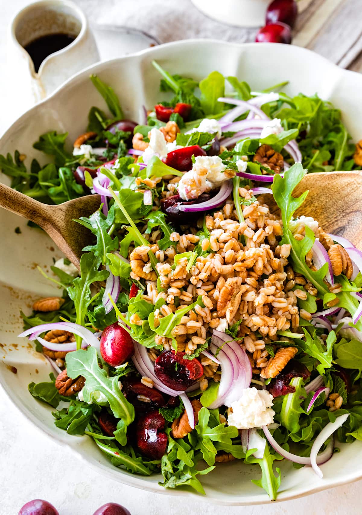 cherry arugula farro salad being tossed with wooden salad servers.