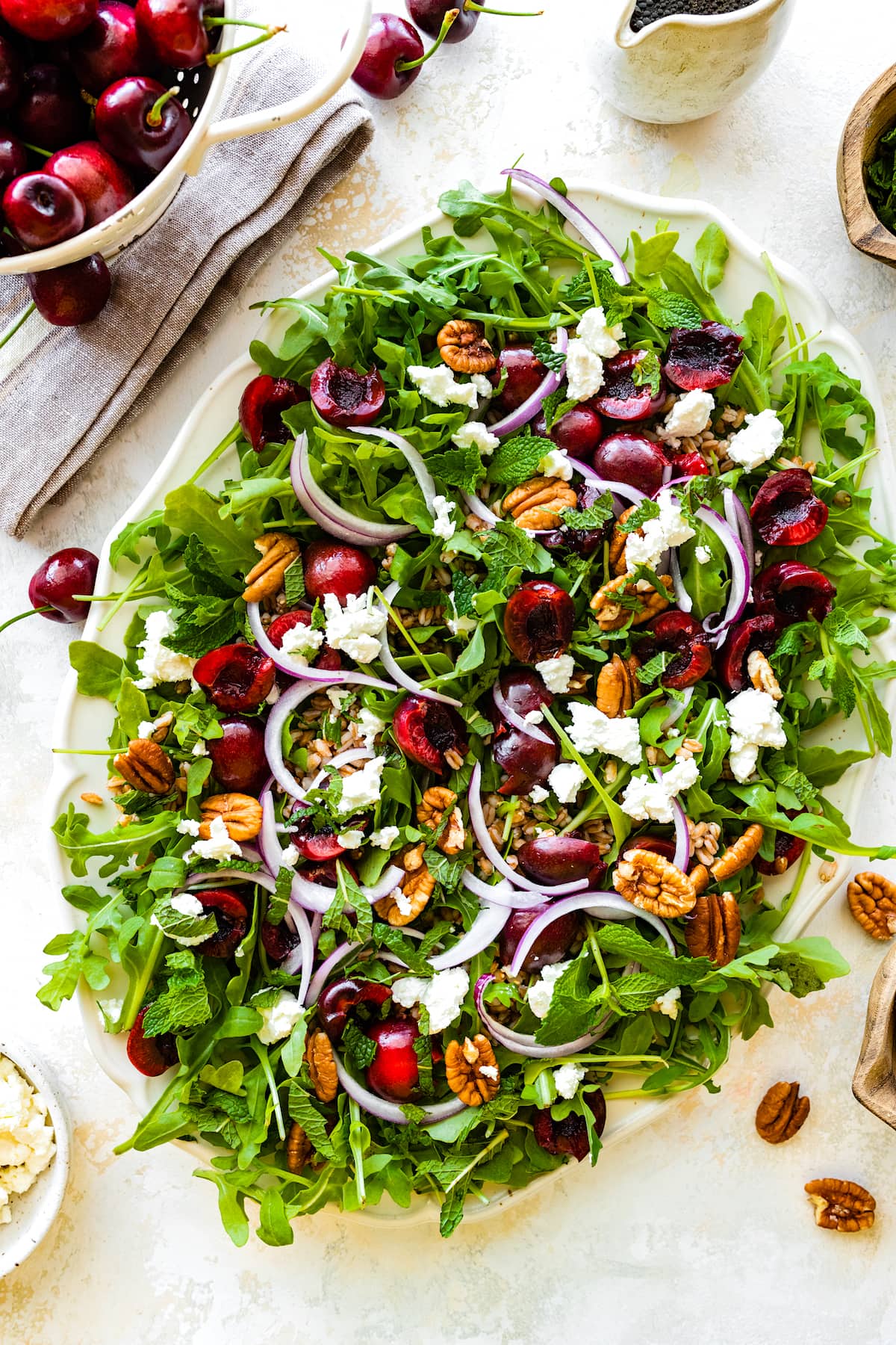 cherry arugula farro salad on platter with goat cheese, red onion, pecans, and mint. 