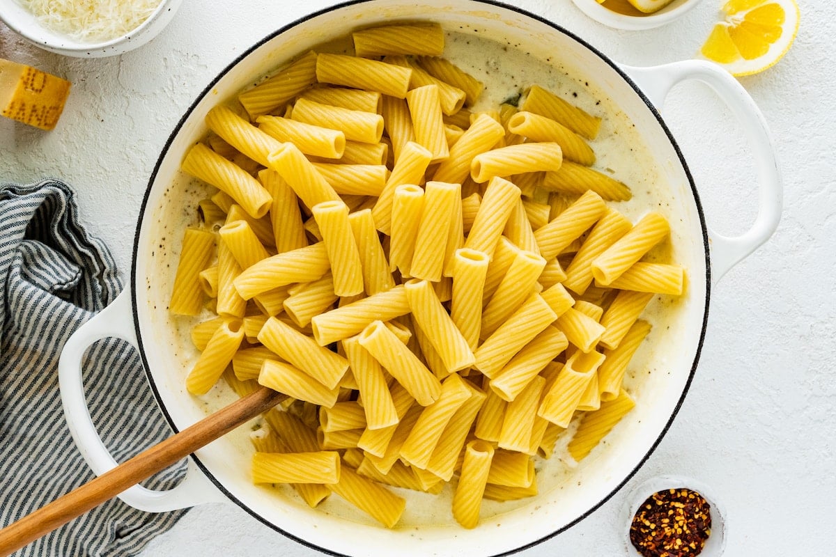 pasta noodles in lemon ricotta sauce in white pot with wooden spoon.