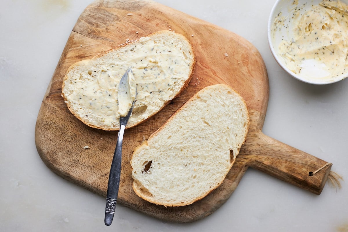 two slices of bread on wood board slathered with garlic butter.