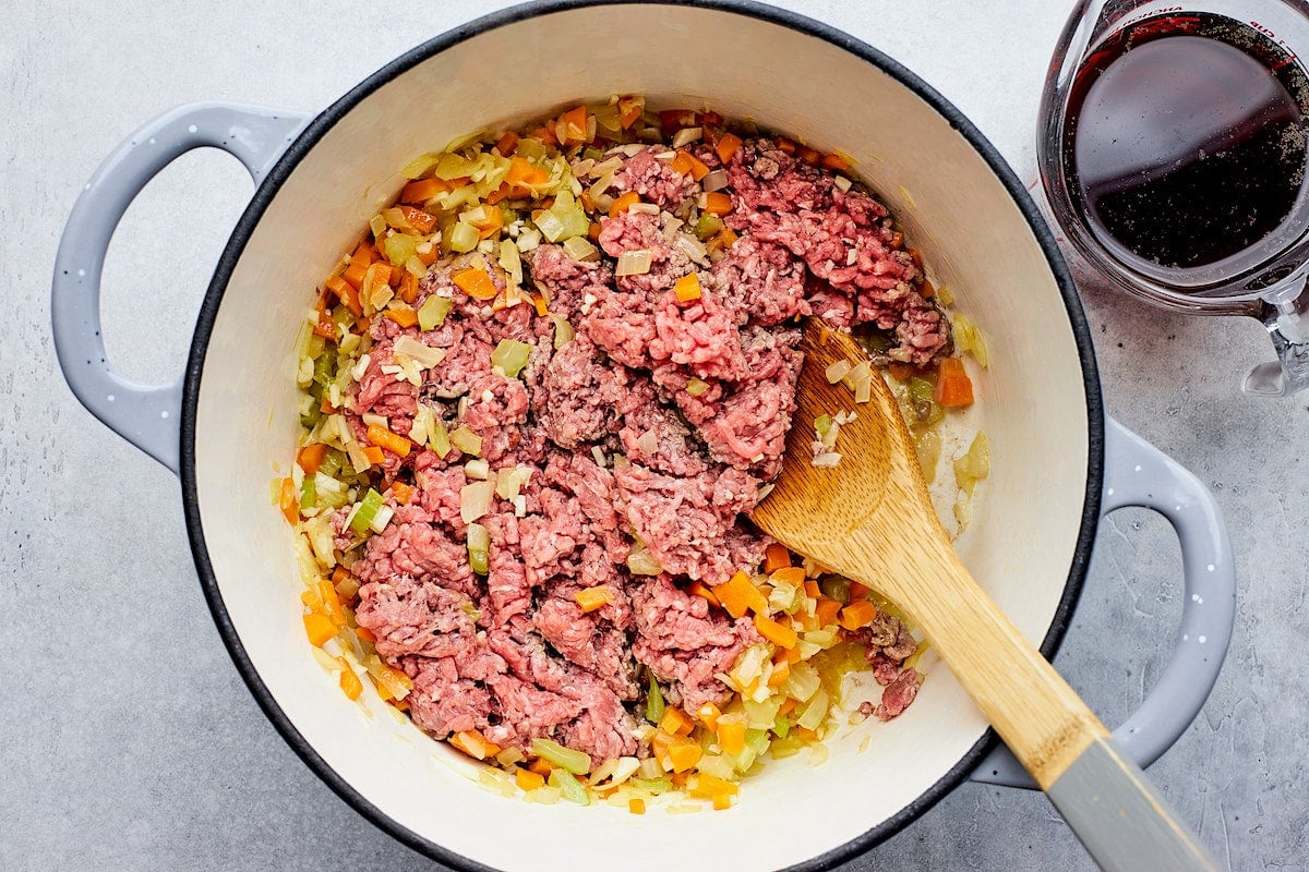 spaghetti meat sauce cooking in pot with wooden spoon.