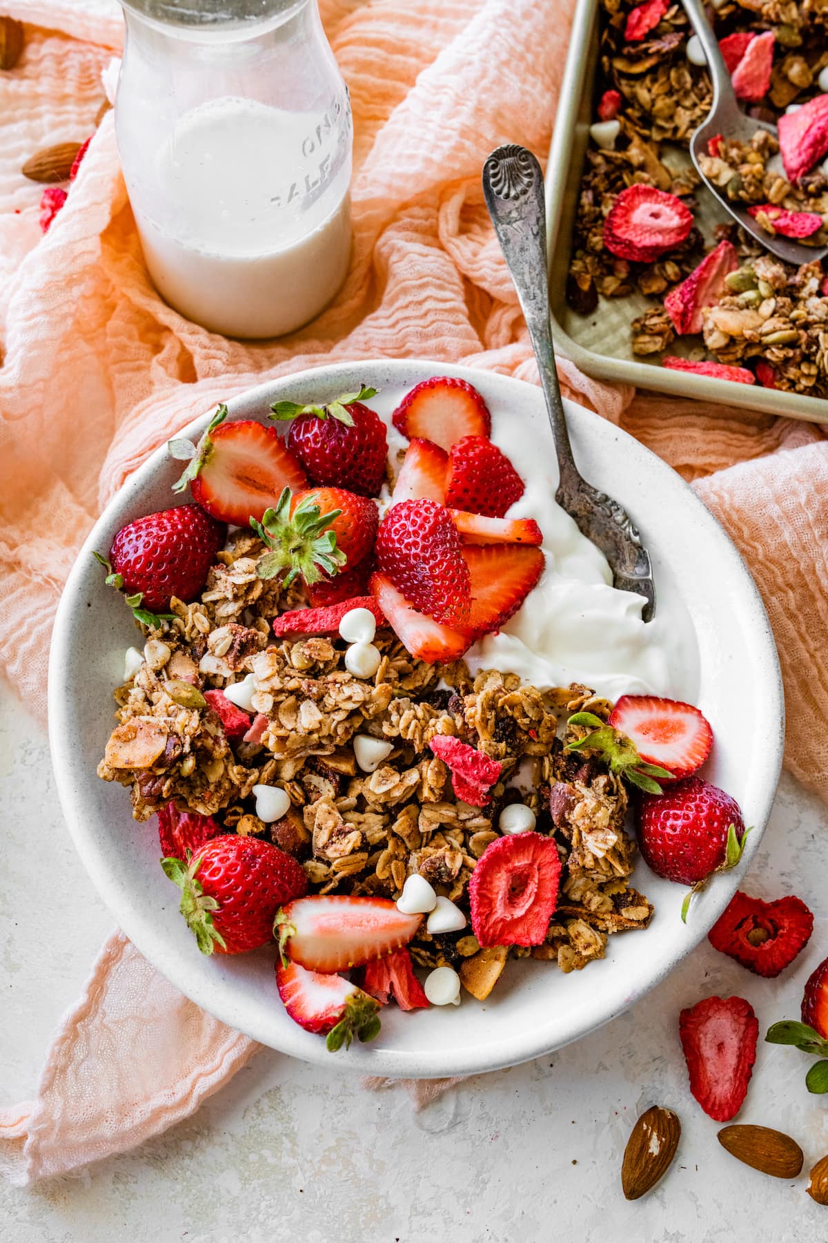 strawberry granola in bowl with yogurt, fresh strawberries, white chocolate chips, and spoon.