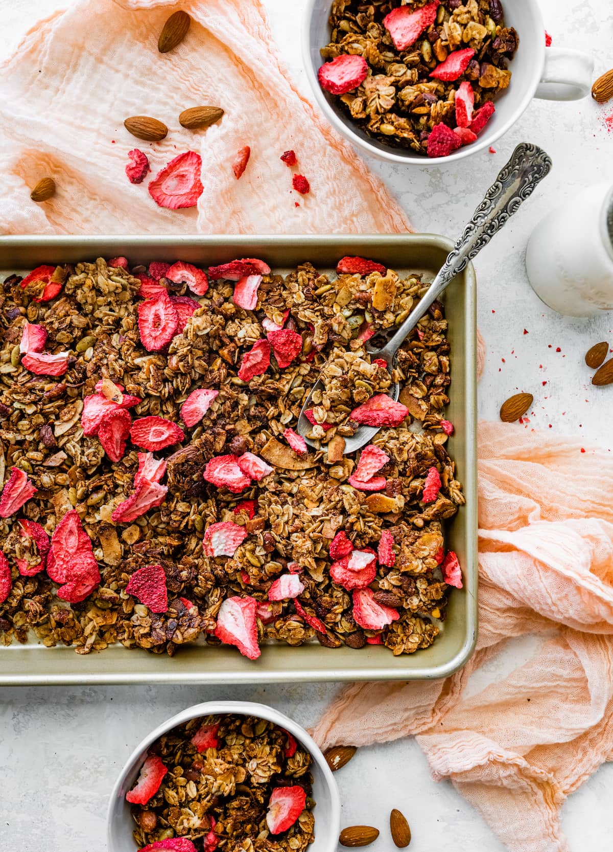 strawberry granola on baking sheet with large spoon.