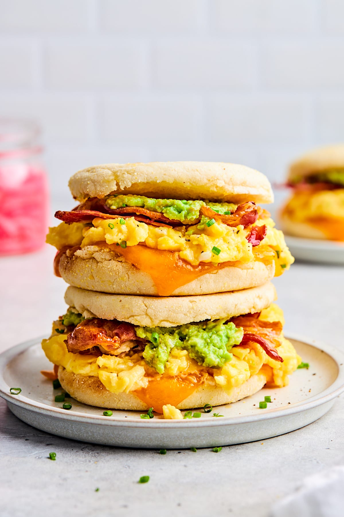 two breakfast sandwiches stacked on top of each other on white plate.