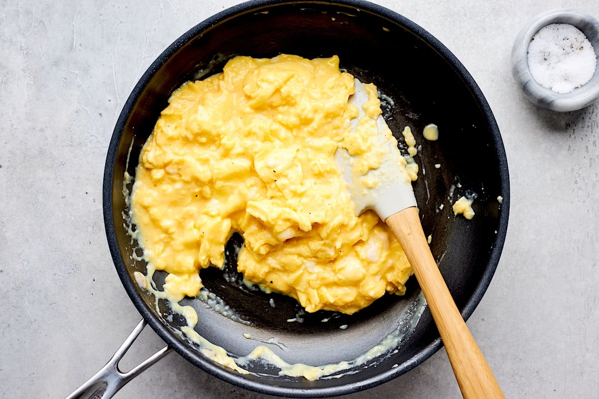 scrambled eggs cooking in skillet with spatula and salt.