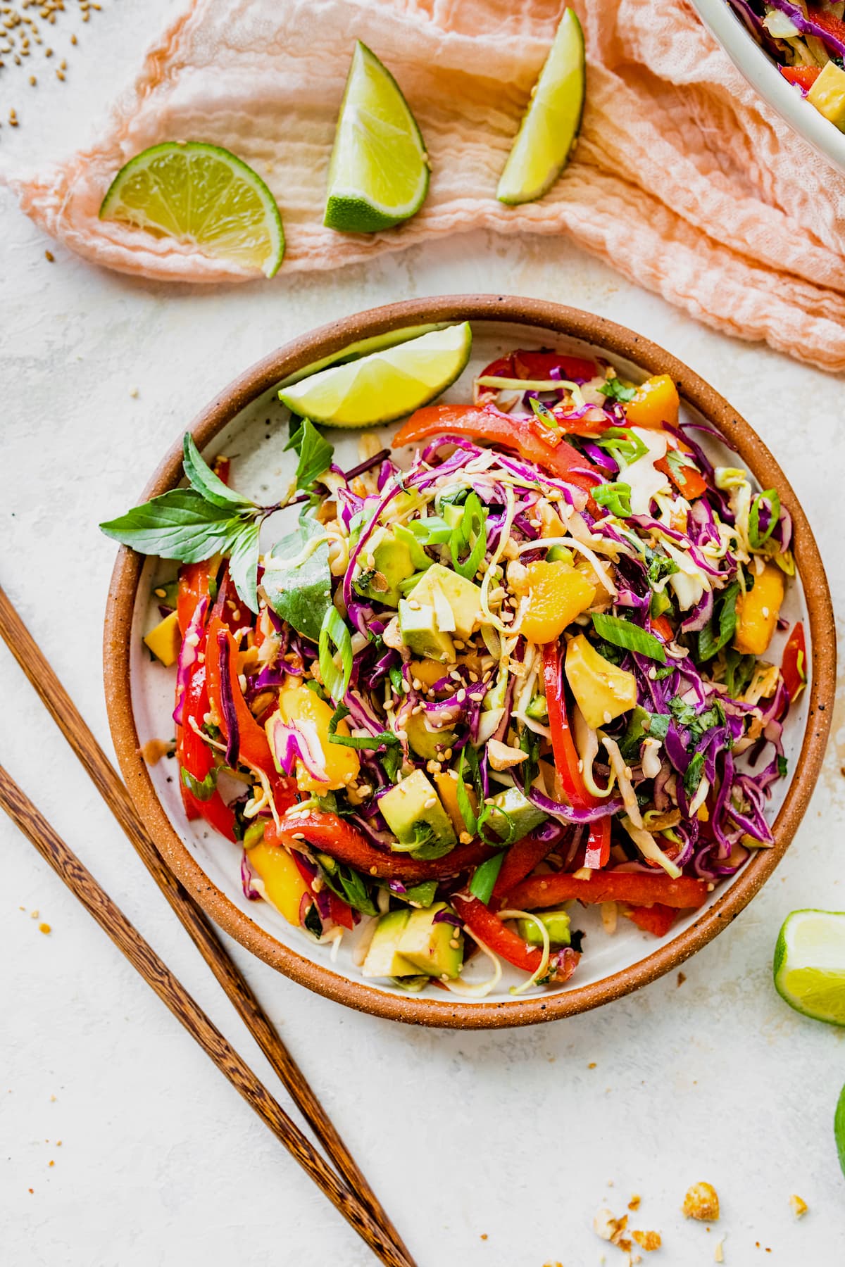 Asian cabbage salad in bowl with chopsticks and lime wedges.