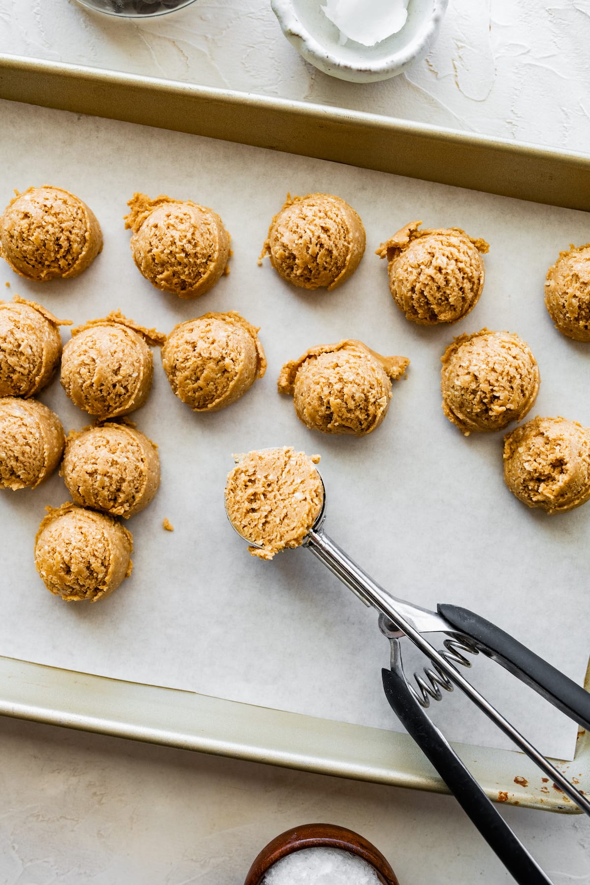 peanut butter protein balls being scooped with cookie scoop on baking sheet with parchment paper.