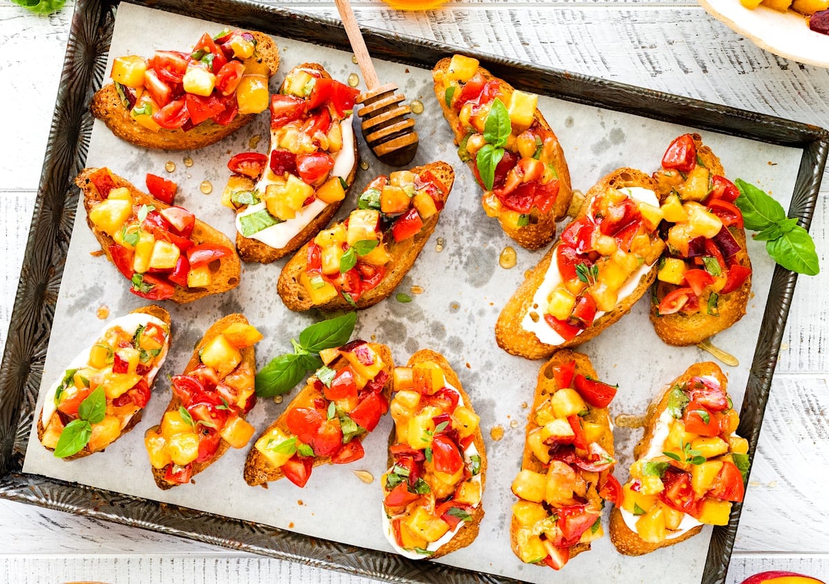 peach tomato bruschetta with drizzle of honey on baking sheet with parchment paper.