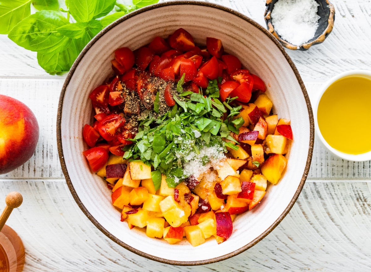 chopped peaches, tomatoes, basil, salt, and pepper in bowl.
