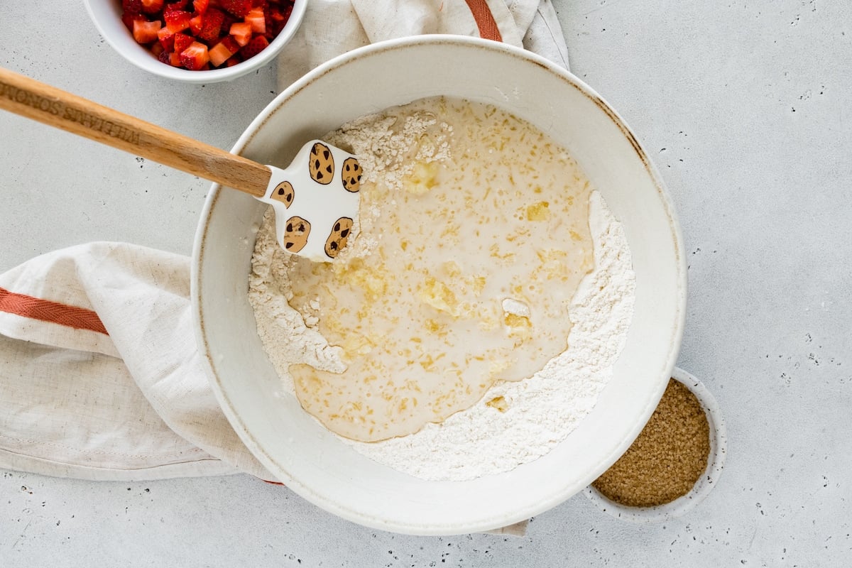 butter and buttermilk mixture being mixed with dry ingredients in bowl with spatula to make drop biscuits.