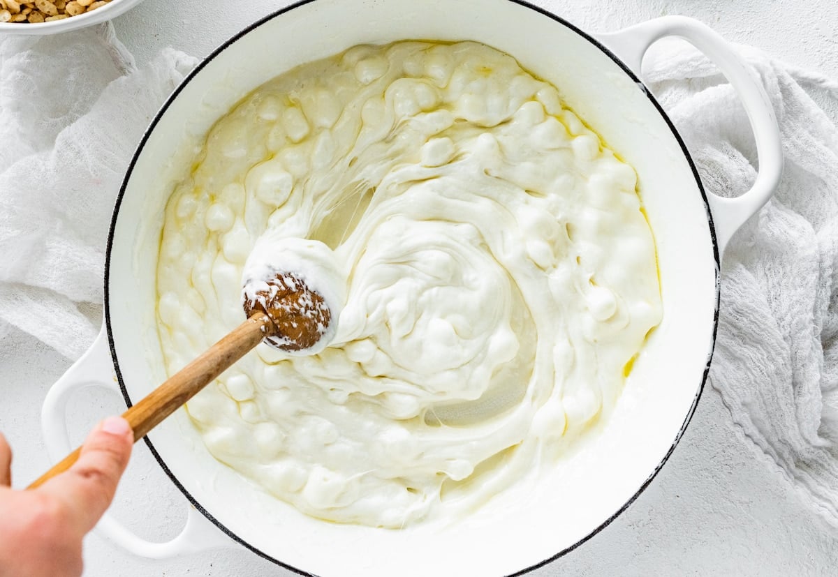stirring melted marshmallows in large white pot with wooden spoon.