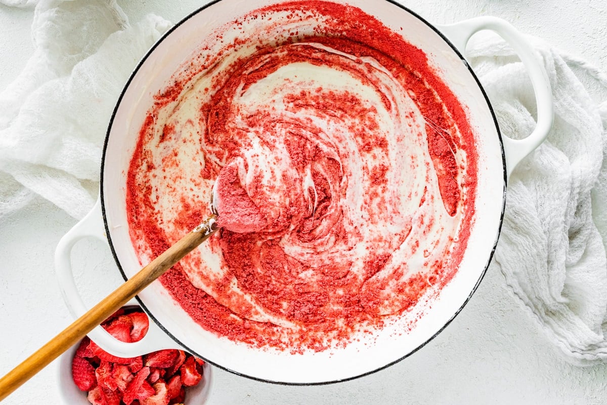 freeze dried strawberry powder stirring into melted marshmallows with wooden spoon in large pot.