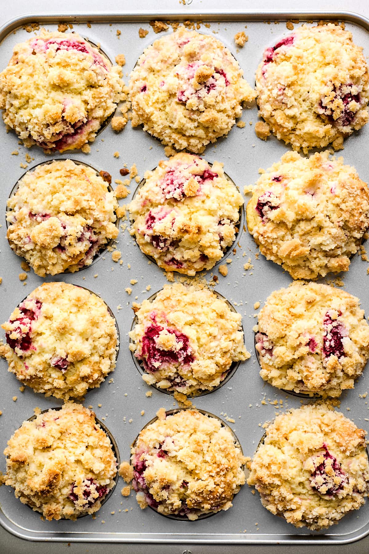 baked raspberry muffins with streusel topping in muffin pan.