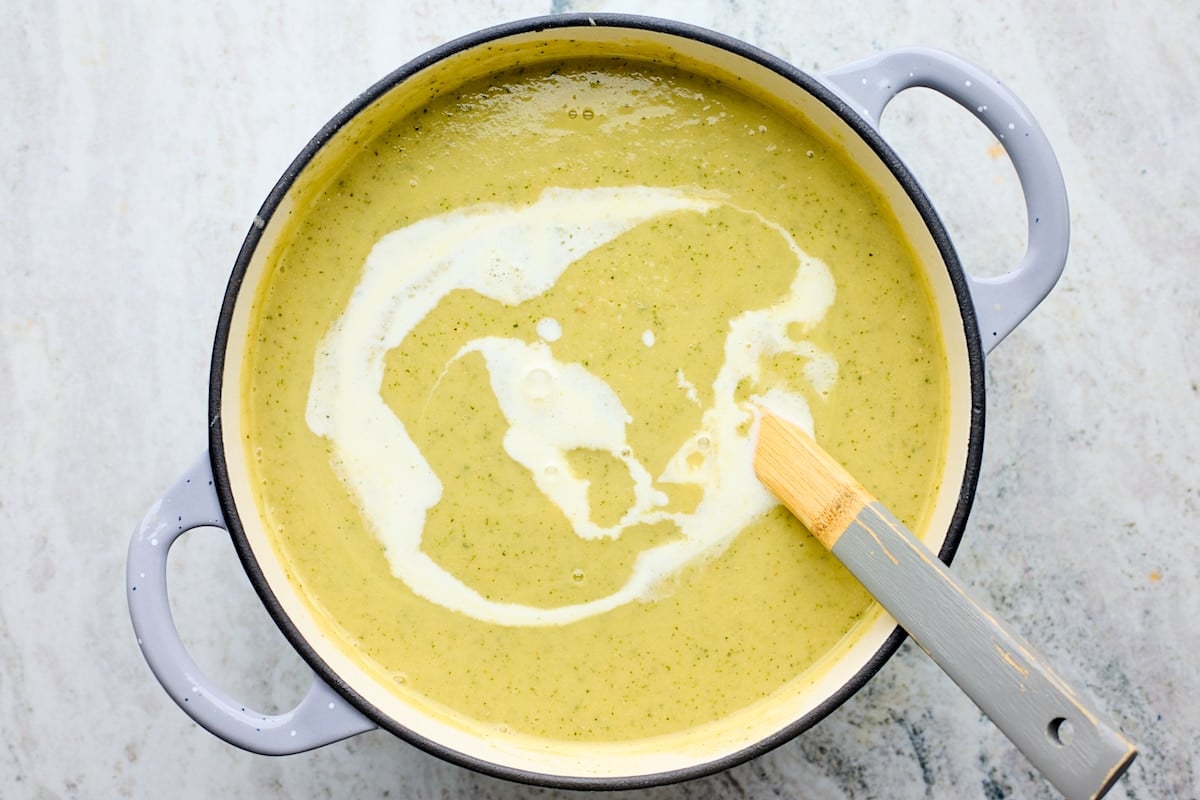 zucchini soup in pot with a drizzle of heavy cream and ladle.