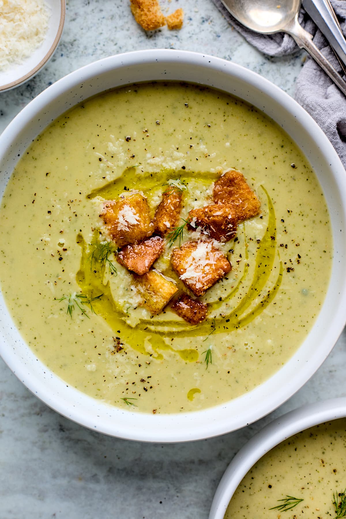 zucchini soup in bowl with black pepper, dill, homemade croutons, and Parmesan cheese.