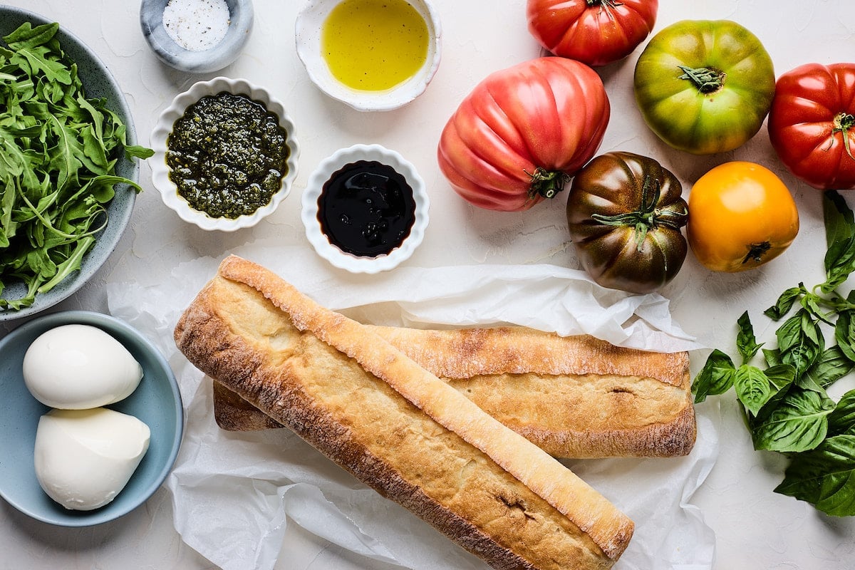 ciabatta bread, fresh mozzarella, pesto, arugula, tomatoes, balsamic, olive oil, and basil to make caprese sandwich.