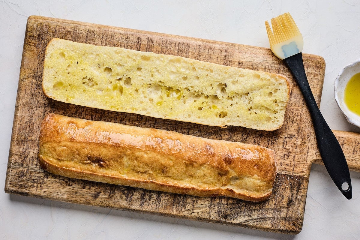 ciabata bread cut in half and brushed with olive oil on wood board.