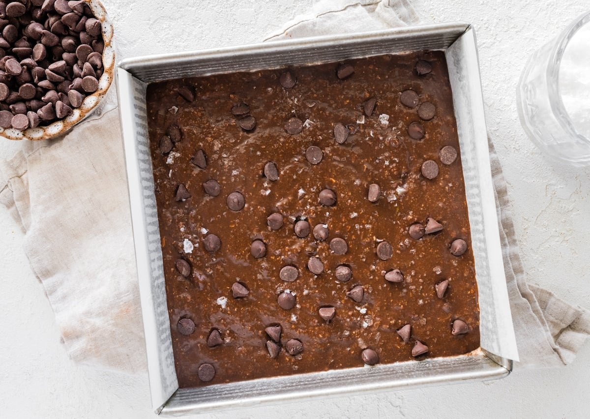 chocolate zucchini snack cake batter in pan with chocolate chips and flaky sea salt.