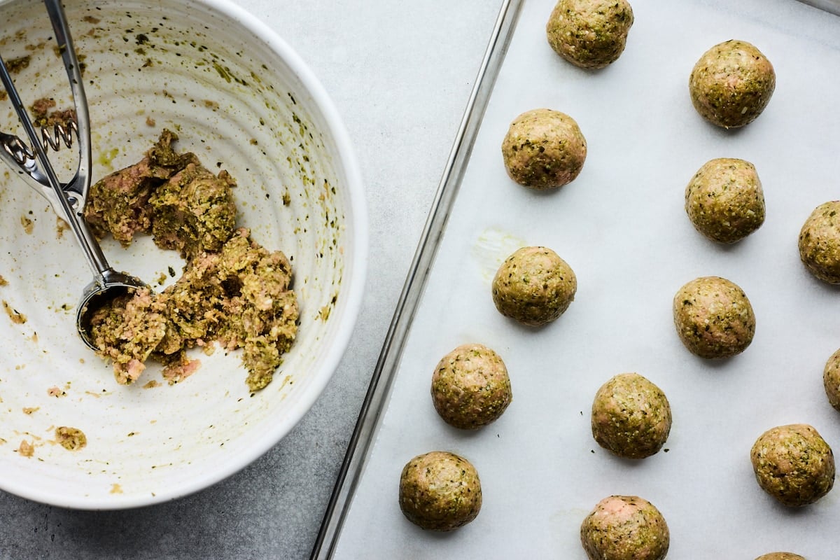 pesto meatballs being scooped onto baking sheet.