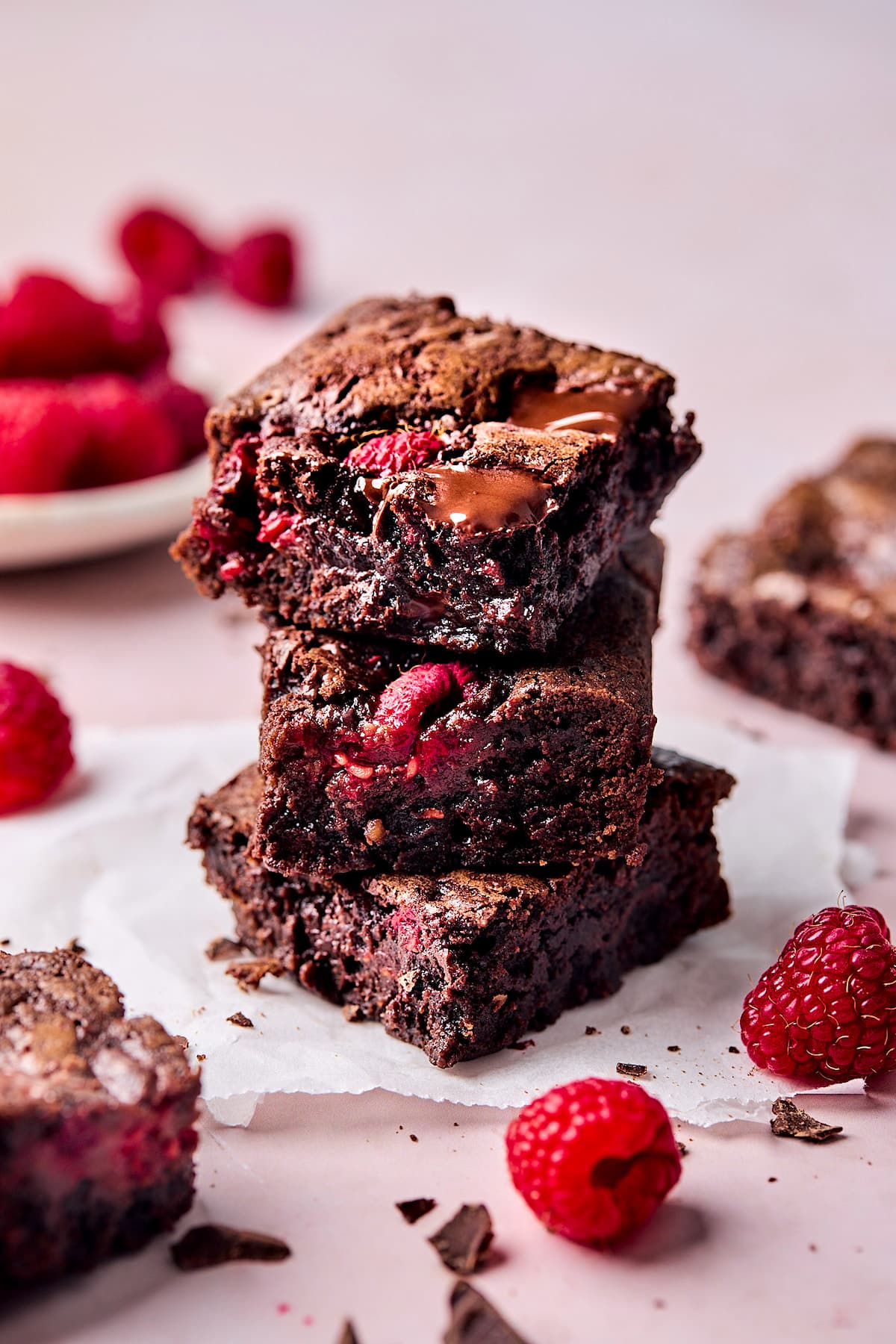 three raspberry brownies stacked on parchment paper.