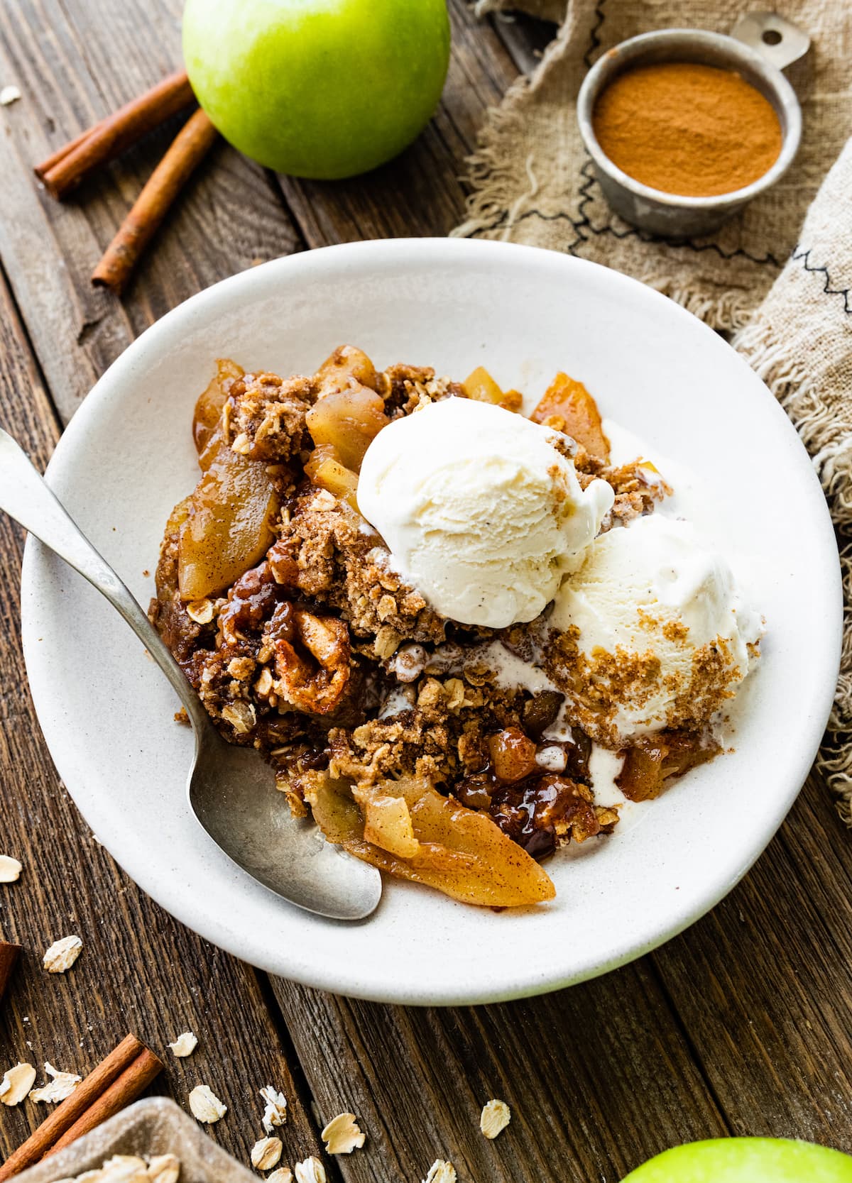 apple crisp with vanilla ice cream in white bowl with spoon.