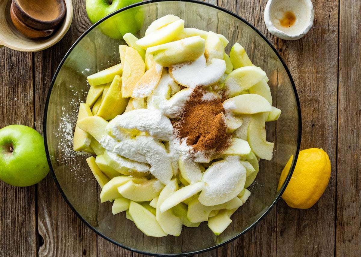 apple slices in large mixing bowl with lemon, flour, cinnamon, and sugar.