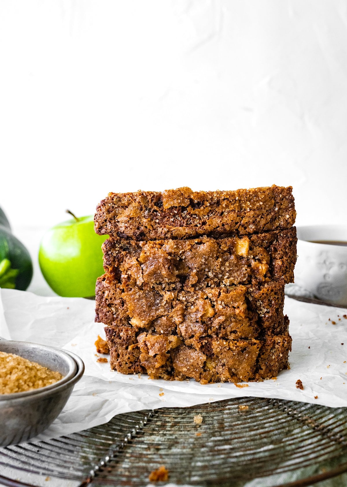 apple zucchini bread slices stacked on parchment paper on cooling rack.