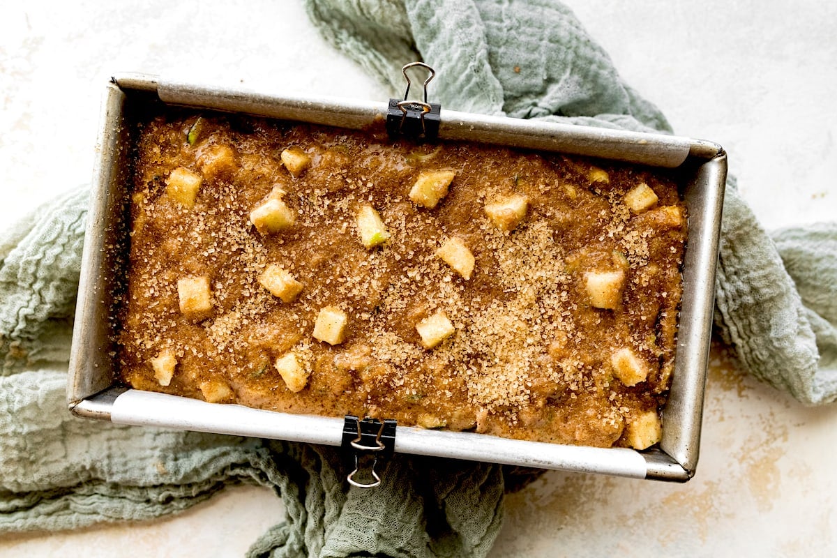 apple zucchini bread batter in loaf pan with tea towel.