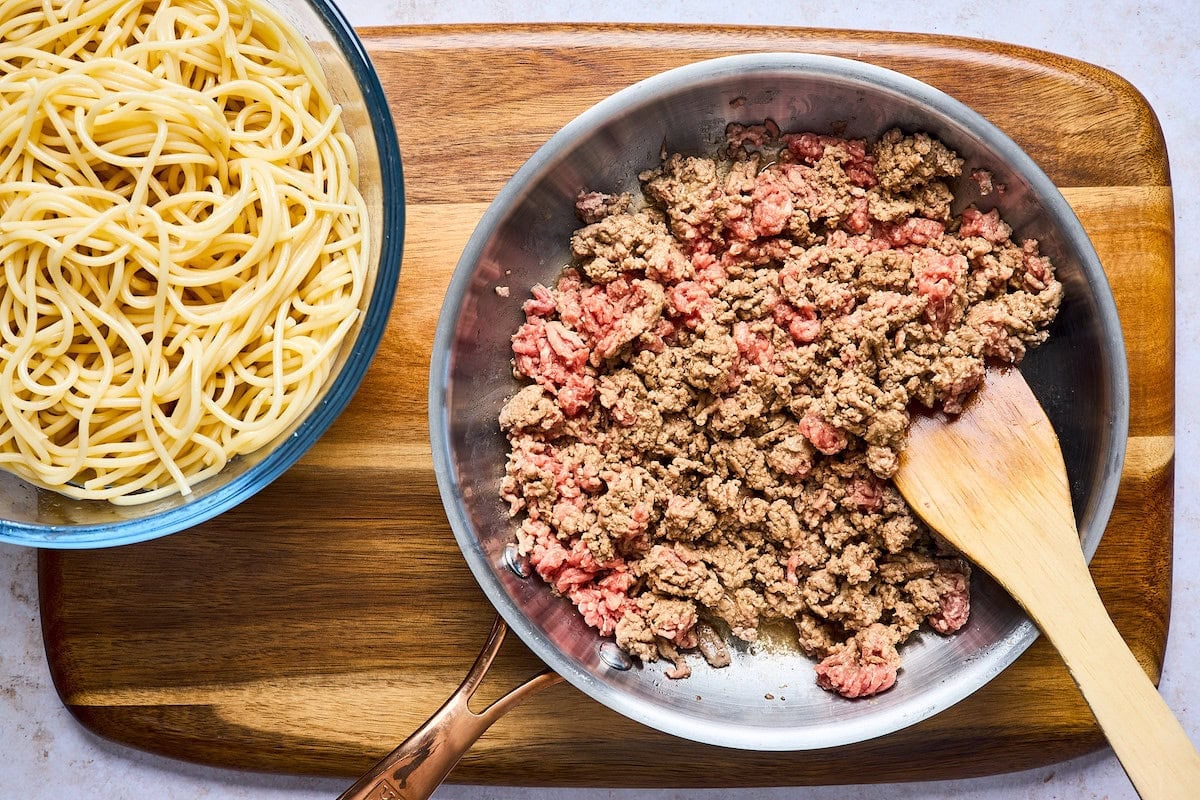 cooked spaghetti in bowl and ground beef cooking in skillet to make baked spaghetti.