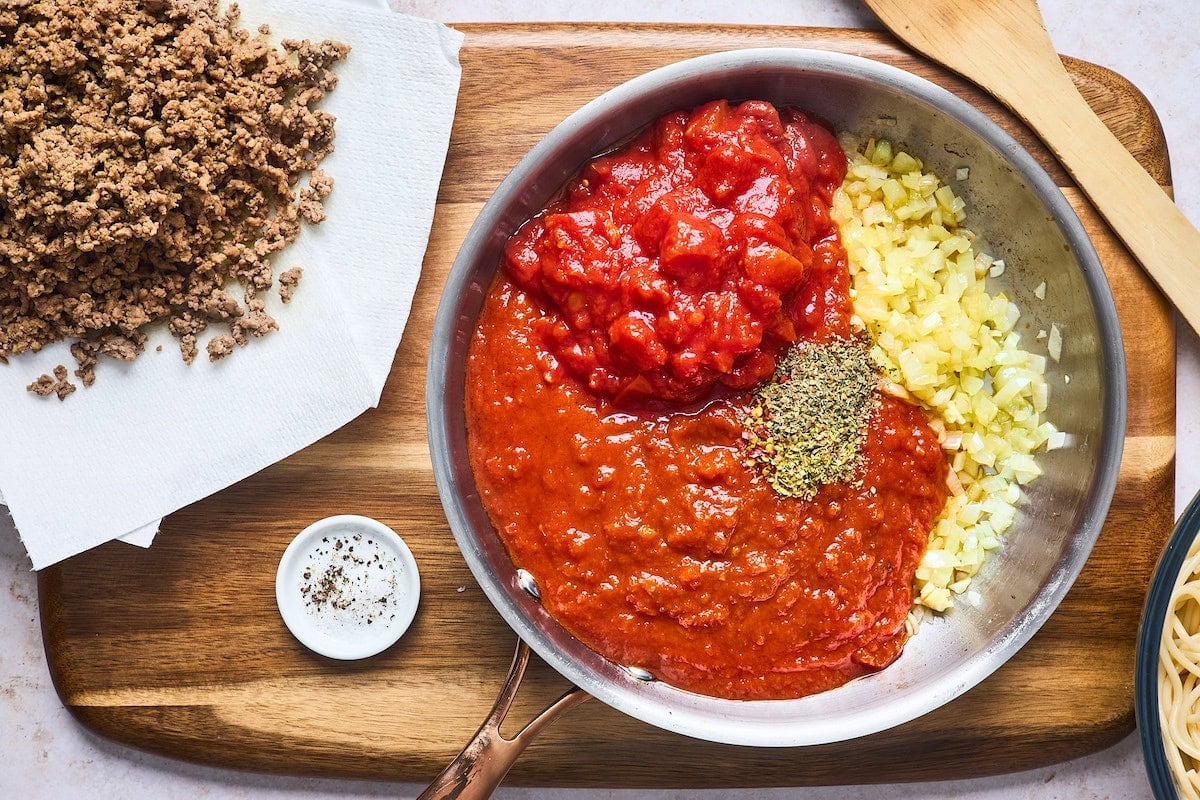 marinara sauce, tomatoes, onion, garlic, and seasonings in skillet with cooked ground beef on the side.