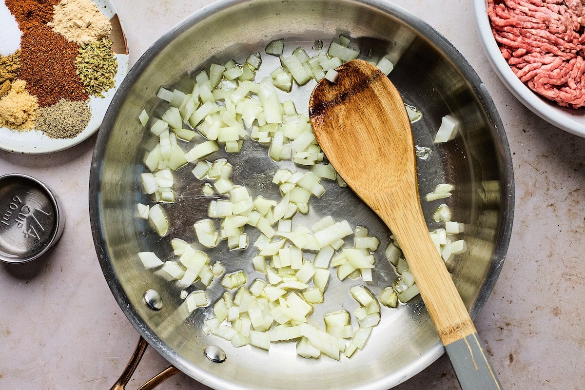 onions cooking in skillet with wooden spoon.