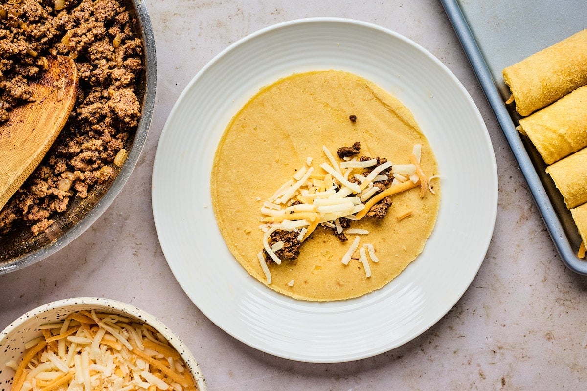 tortilla on plate with beef and cheese to make beef taquitos.