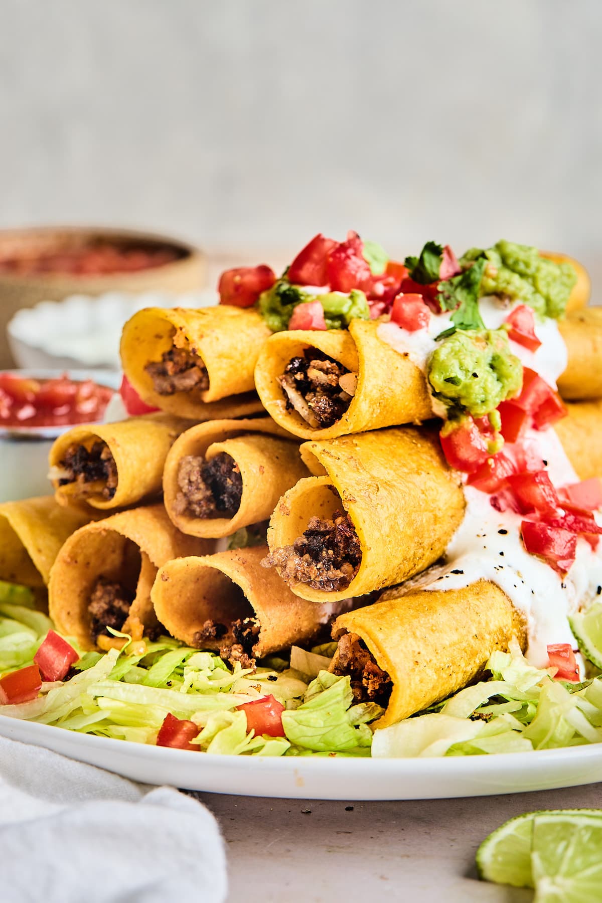 stack of beef taquitos on platter with shredded lettuce and tomatoes.