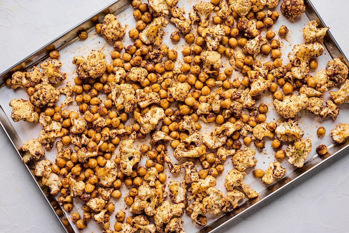 cauliflower and chickpeas tossed in spices on baking sheet with parchment paper.
