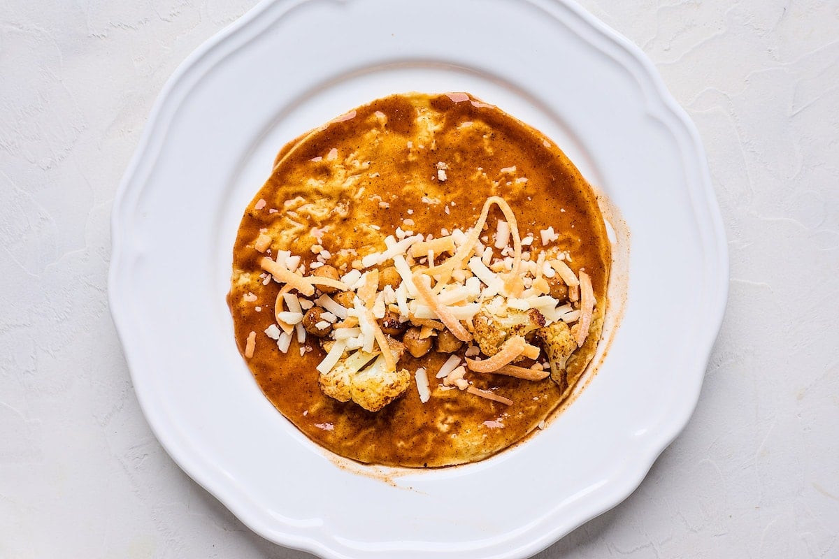 corn tortilla dipped in enchilada sauce being filled with roasted cauliflower, chickpeas, and cheese.