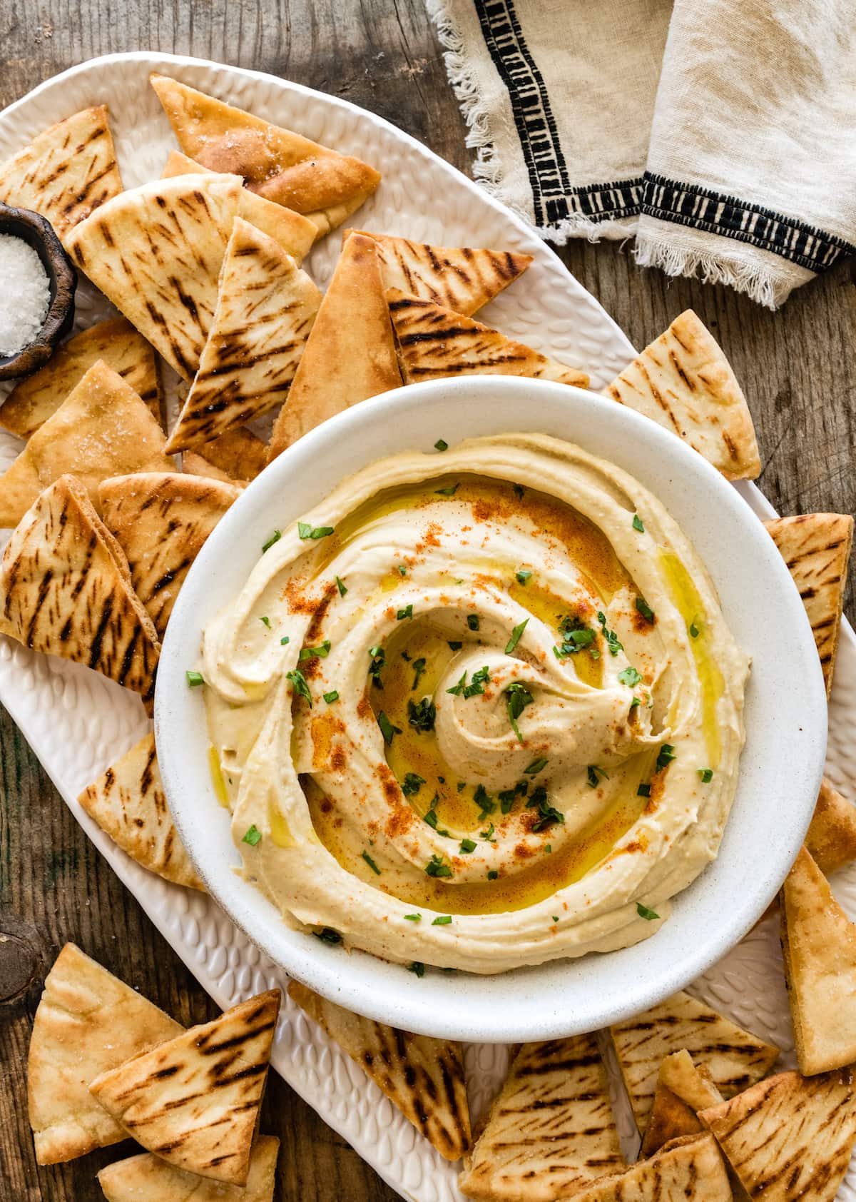 hummus in serving bowl with pita chips on platter.