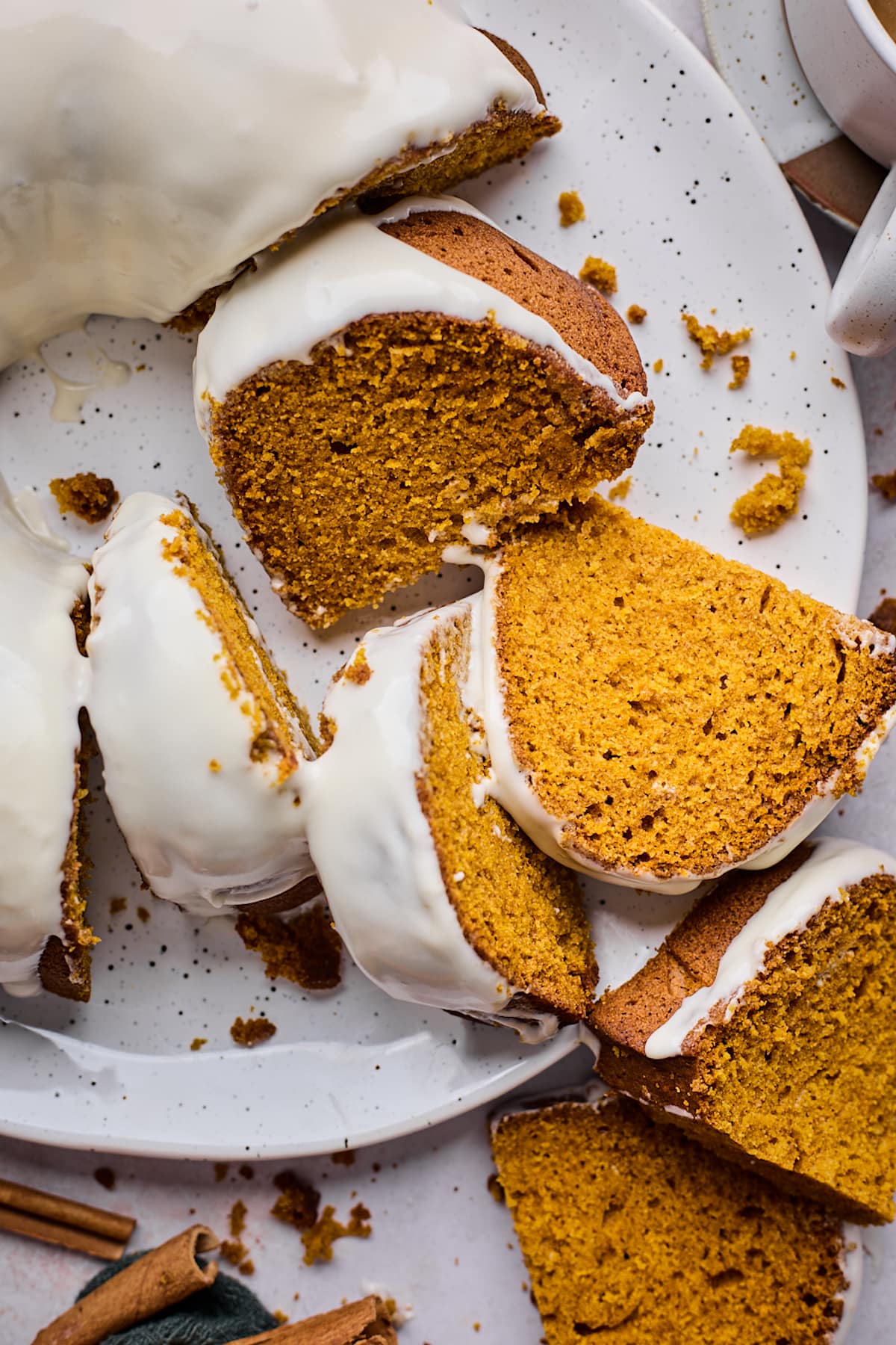 pumpkin bundt cake with cream cheese frosting cut into slices on platter.