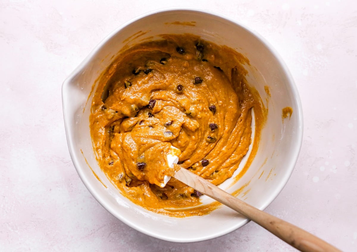 pumpkin chocolate chip muffin batter in mixing bowl with spatula.