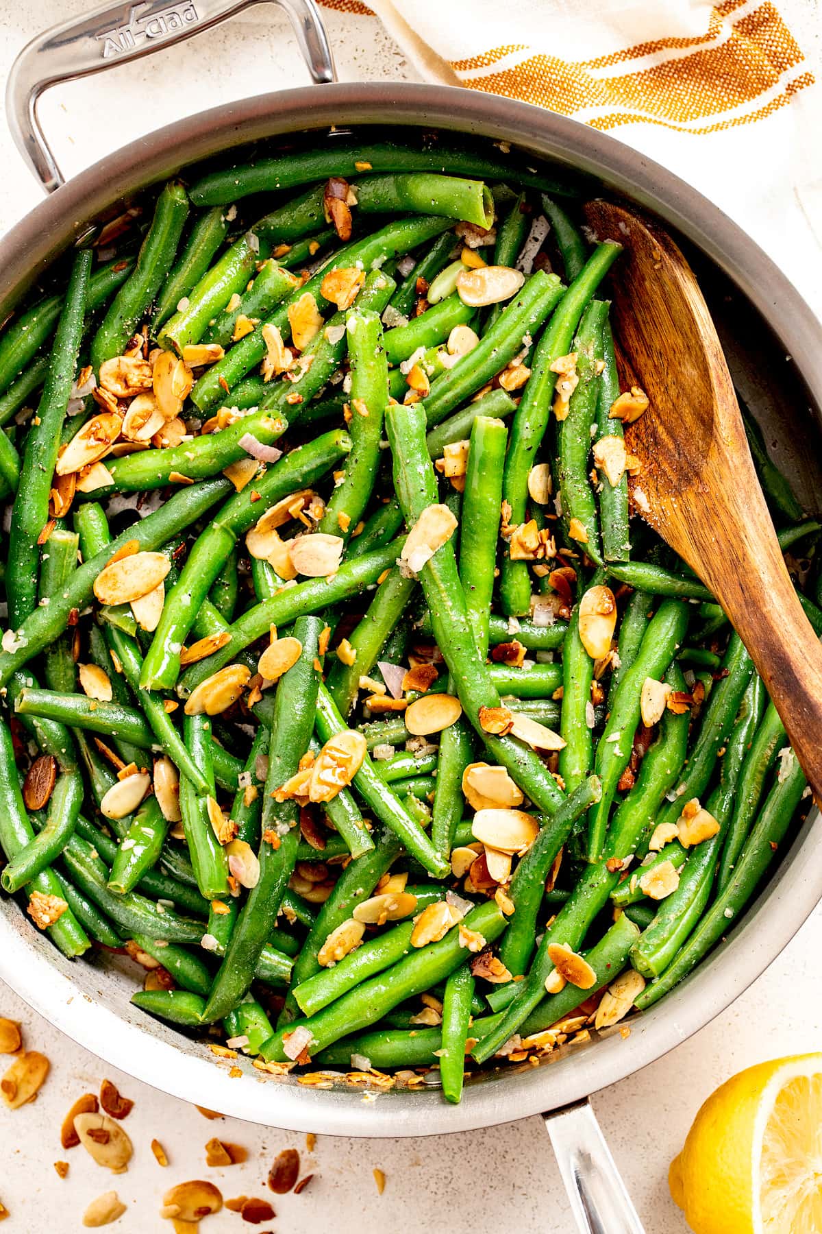 green beans with sliced almonds in large skillet with wooden spoon.