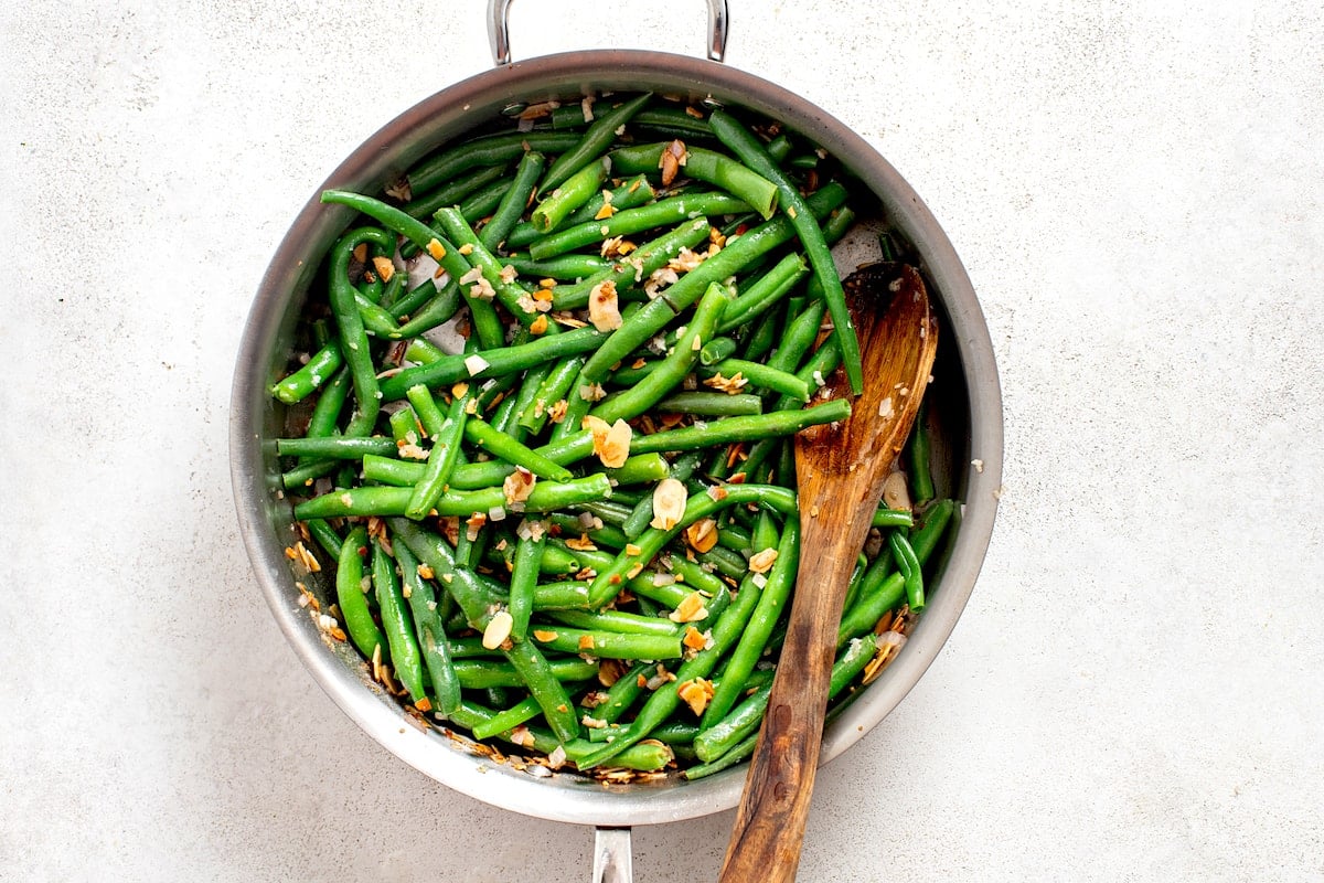 green beans almondine cooking in skillet with wooden spoon.